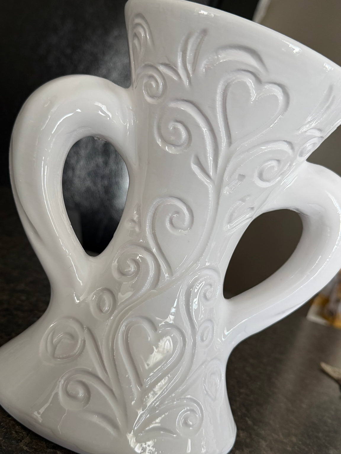 Close-up of white vase with raised vine, scroll, and heart designs