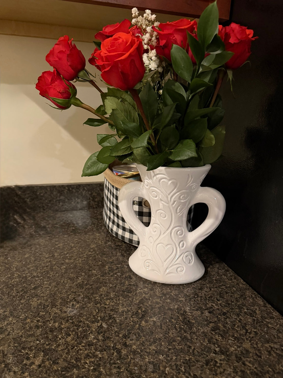 White decorative heart vase shown on a counter with red roses